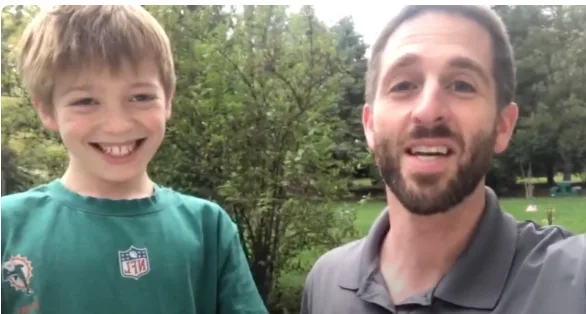 A smiling boy standing beside his father in a backyard video testimonial about silver diamine fluoride treatment
