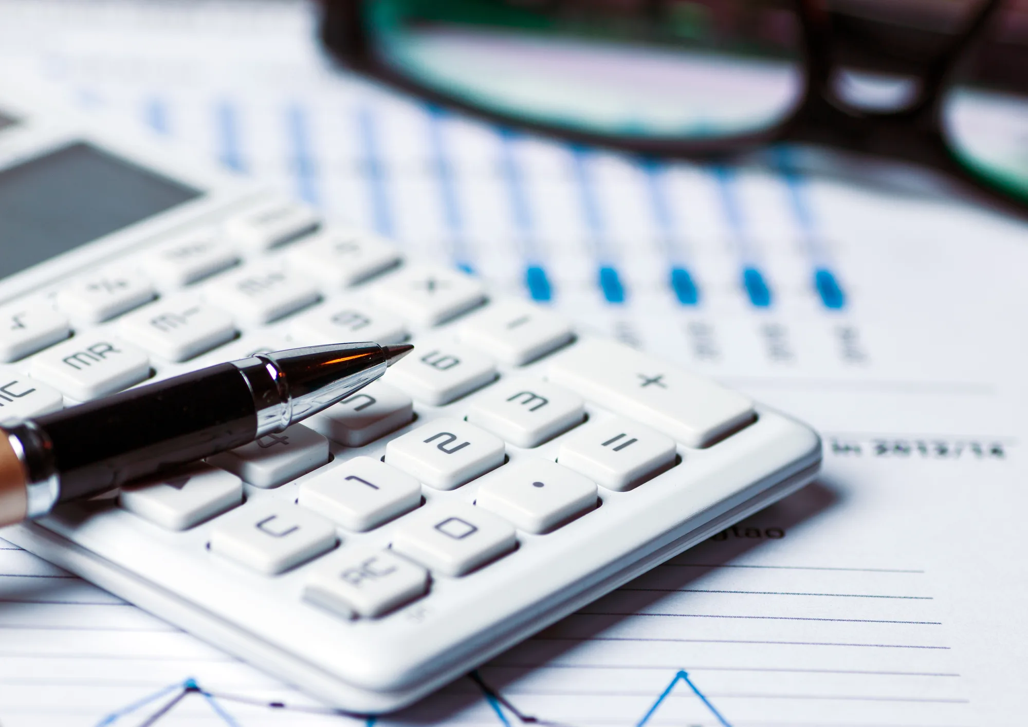 A pen resting on a white calculator atop financial charts, illustrating the cost arithmetic of screening