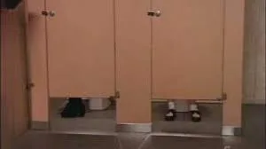 Feet visible under the doors of adjacent public restroom stalls