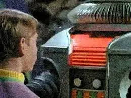 The robot from the TV series Lost in Space beside a cast member, evoking its Danger, Will Robinson warning