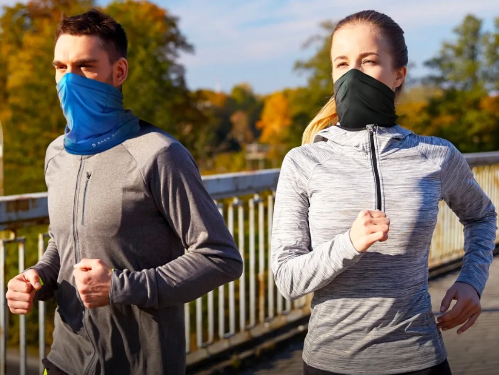 A man and woman jogging outdoors wearing stretch-fabric neck-gaiter face coverings