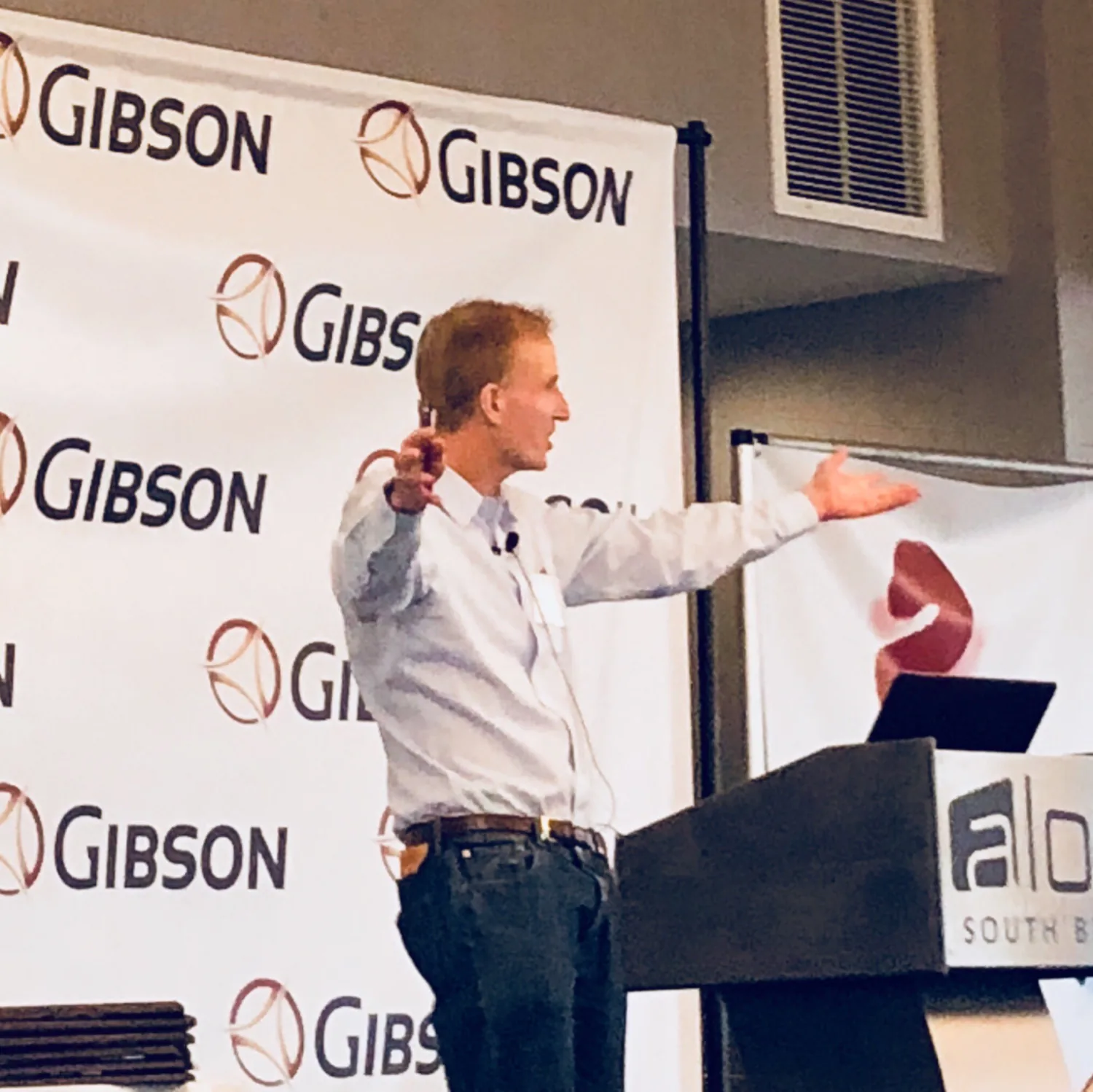 Al Lewis at a lectern mid-question, gesturing to the room at a benefits conference.